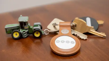 AirTag in a leather key fob next to keys on a wooden table