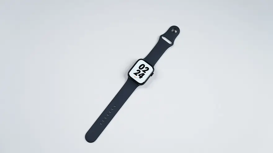 Midnight Apple Watch Series 8 with a dark sport band lying flat on a pale studio surface