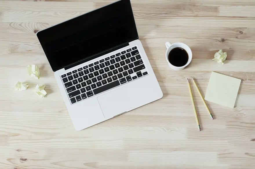 Open laptop next to a cup of coffee on a wooden desk