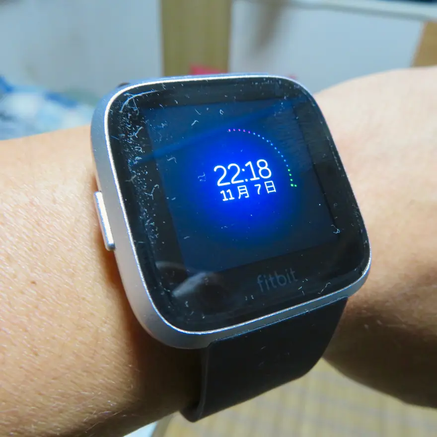 Fitbit Versa smartwatch with a silver case and glowing blue clock face worn on a wrist