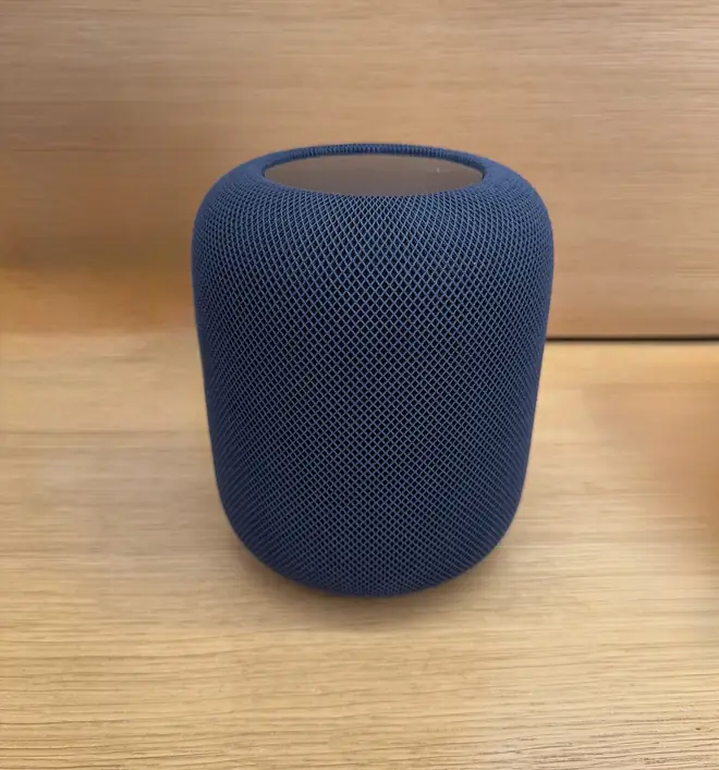Second generation Apple HomePod speaker wrapped in dark mesh fabric on a side table