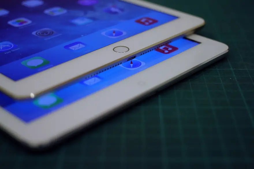 Two gold and white Apple iPad tablets stacked together on a dark green cutting mat