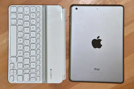 Silver iPad mini next to a small white keyboard on a wood surface