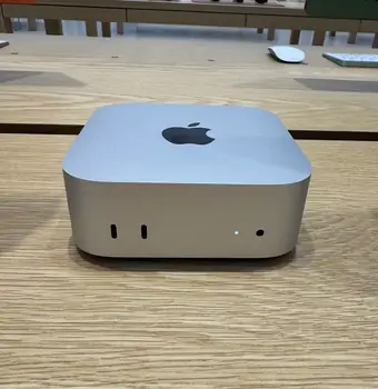 Compact silver Apple Mac mini sitting on a wooden desk surface