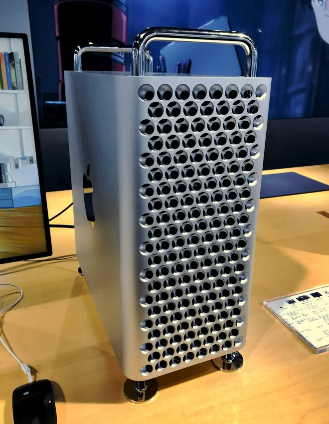 Silver Apple Mac Pro tower with lattice grille, top handles, and wheels beside a wooden desk