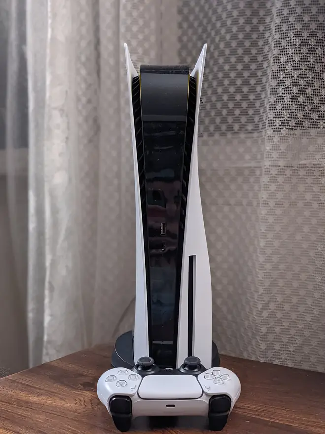 White Sony PlayStation 5 console standing vertically with a DualSense controller in front