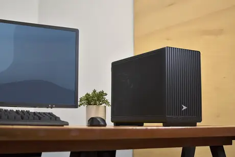 Compact black business desktop computer beside a monitor on a wooden desk