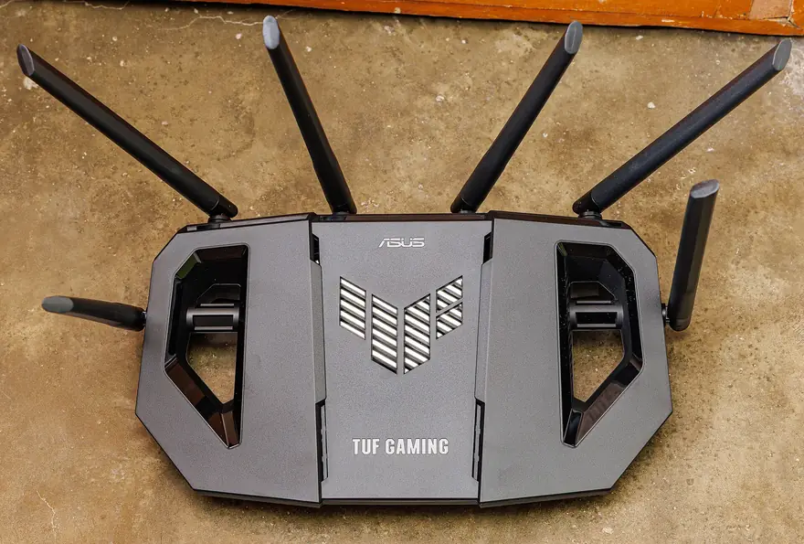 Black ASUS TUF Gaming router with six antennas laid out on a concrete floor