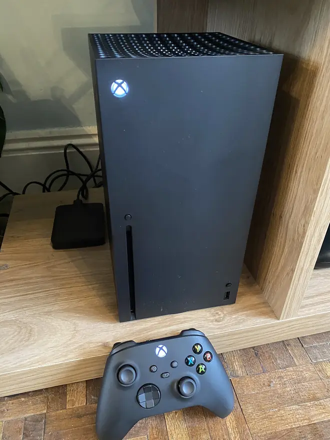 Black Xbox Series X tower console standing upright with a wireless controller nearby